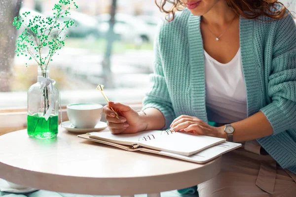 Mavi, sıcak kazaklı genç bir kadın büyük bir kahve dükkanının penceresinde oturmuş notlar yazıyor.