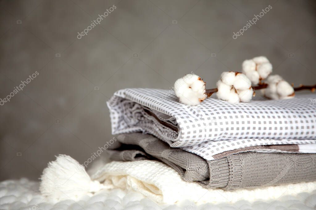 Stack of folded warm blankets with different design patterns and cotton branch on grey background. Knitted blankets. Production of natural plant-based textile fibers. Manufacture. Organic product