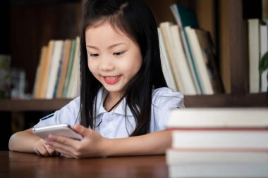 Şirin kız gülümsüyor kütüphanede akıllı telefon oynuyor, çocuk konsepti, eğitim konsepti