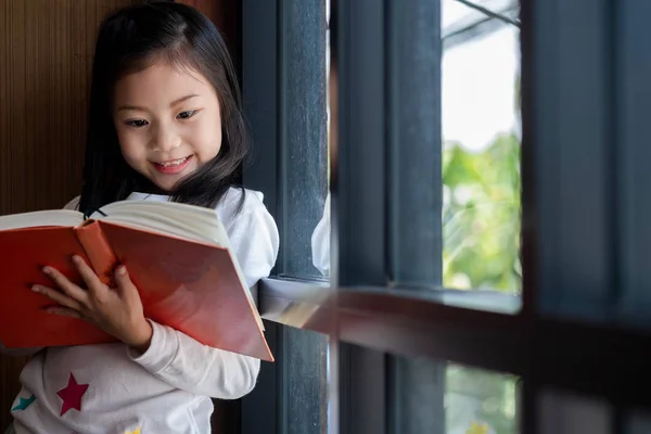 かわいい女の子は笑顔で図書館の本を読んで立って子供の概念教育の概念 — ストック写真
