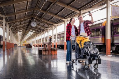 Birlikte tatilde olan mutlu genç çiftler tren istasyonunda telefonla selfie çekiyorlar, seyahat konsepti, çift konsepti. 