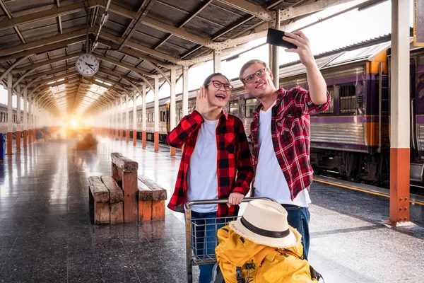 Birlikte tatilde olan mutlu genç çiftler tren istasyonunda telefonla selfie çekiyorlar, seyahat konsepti, çift konsepti. 