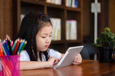 Şirin kız gülümsüyor ve kütüphanede tablet akıllı telefon oynuyor. Çocuk konsepti, eğitim konsepti.