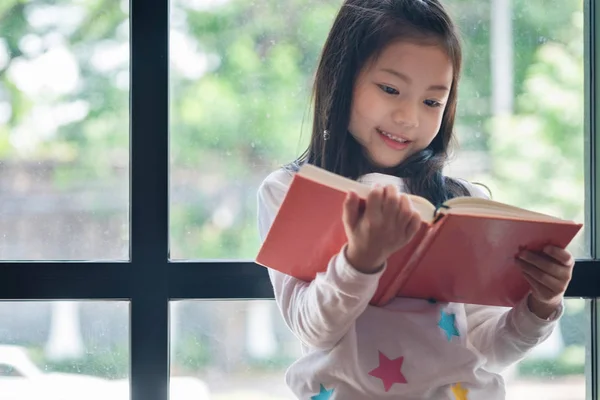 かわいい女の子は笑顔で図書館に立って読書をしていました子供の概念教育の概念 — ストック写真