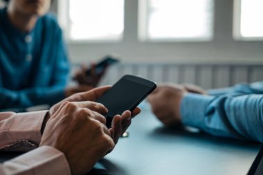 Genç iş adamları ahşap masa üzerinde akıllı telefon kullanıyor.