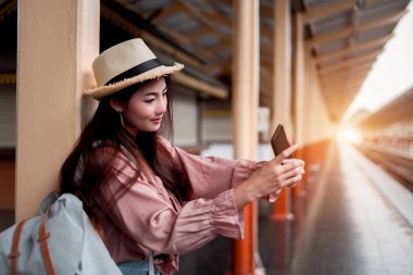 Sırt çantalı, gülümseyen kadın gezgin. Elinde akıllı telefon var.