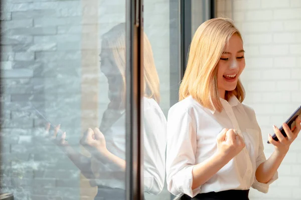 Junge Geschäftsfrau steht am Bürofenster und lächelt in die Arme — Stockfoto