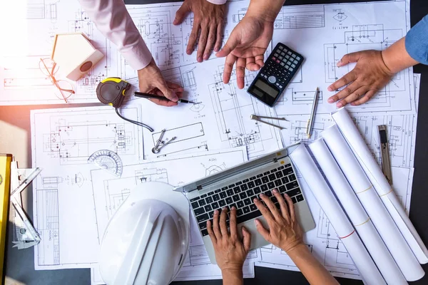 Engineers pointing to building on blueprint and using laptop to — Stock Photo, Image
