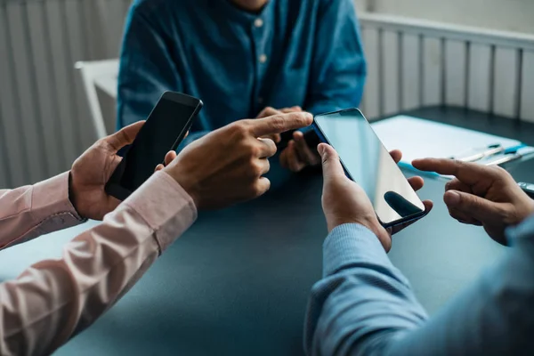 Genç iş adamları ahşap masa üzerinde akıllı telefon kullanıyor.