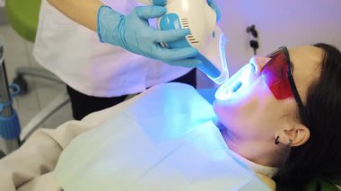 Modern bir diş kliniğinde morötesi diş beyazlatma prosedürü. Doktor hastaların dişlerini beyazlatır. Kozmetik dişçiliği.