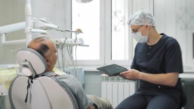 Bir dişçi bir hastaya tablette çenelerinin röntgenini gösterir. Modern bir diş kliniğinde hasta danışmanlığı.