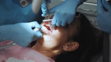 Dişçide genç bir kadın. Bir dişçi ve bir asistan, modern bir klinikte dişçi koltuğunda yatan bir hastanın dişlerini tedavi eder..