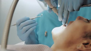 Dişçide genç bir kadın. Bir dişçi ve bir asistan, modern bir klinikte dişçi koltuğunda yatan bir hastanın dişlerini tedavi eder..
