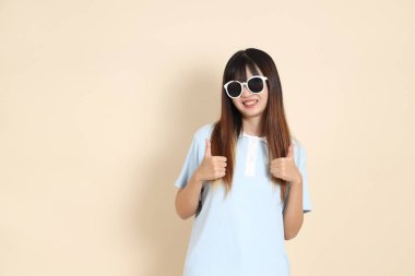 Mavi polo tişört giyen Asyalı bir kadın, beyaz şort, güneş gözlüğü, baş parmak, tamam mı? Üniversite öğrencisi, Gen Z, Summer