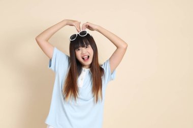 Asyalı bir kadın mavi polo gömlek, beyaz şort, güneş gözlüğü, kalp şeklinde mini kalp, bej arka planda aşk. Üniversite öğrencisi, Gen Z, Summer