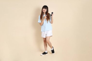 Asyalı bir kadın mavi polo gömlek, beyaz şort, güneş gözlüğü takıyor, bej bir arka planı işaret ediyor. Üniversite öğrencisi, Gen Z, Summer