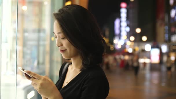 Asiática joven utilizando el teléfono móvil en la calle, 4k — Vídeo de stock