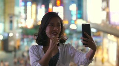 Bir güzel genç Çinli kız video şehir sokak gece cep telefonu kullanarak arkadaşı ile sohbet, 4k