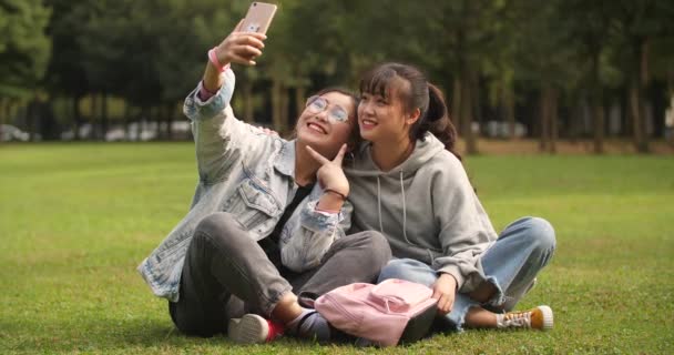 Две азиатки из колледжа используют мобильный телефон, чтобы сделать селфи в кампусе — стоковое видео