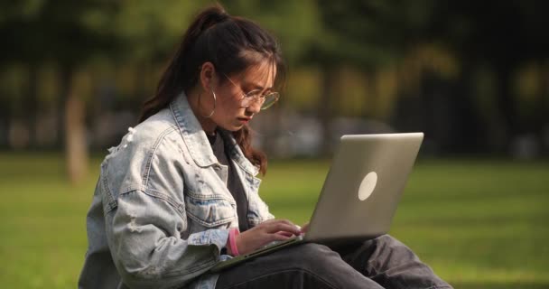 Ασιατικό κορίτσι κολλέγιο απασχολημένος χρησιμοποιώντας φορητό υπολογιστή στο γκαζόν στο Πανεπιστήμιο — Αρχείο Βίντεο