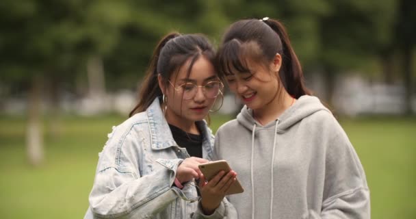 Δύο ασιατικό κορίτσι κολλέγιο κοιτάζοντας το κινητό τηλέφωνο στην πανεπιστημιούπολη — Αρχείο Βίντεο