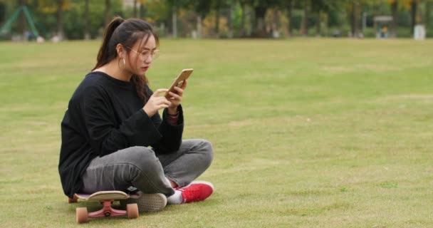 Asiática chica universitaria utilizando el teléfono móvil en el césped en el campus — Vídeo de stock