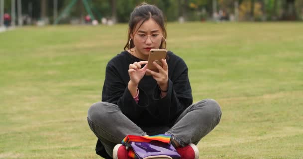 Ασιατικό κορίτσι κολλέγιο χρησιμοποιώντας το κινητό τηλέφωνο στο γκαζόν στο Πανεπιστήμιο — Αρχείο Βίντεο