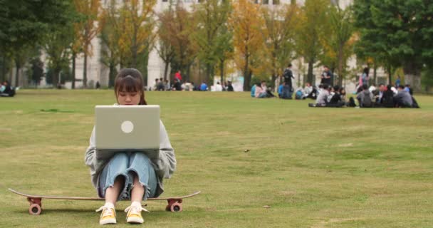 Asijská studentka používající přenosný počítač na trávníku — Stock video