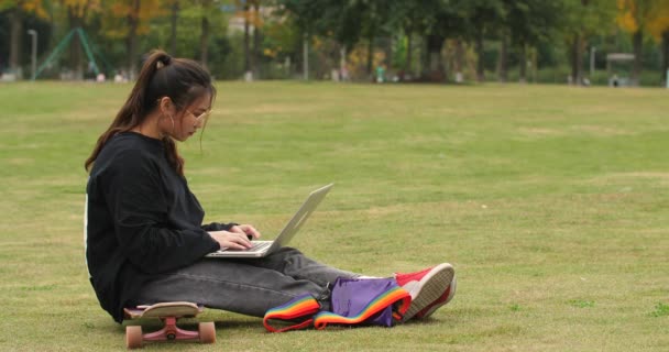 Ασιατικό κορίτσι κολλέγιο κάθεται στο σκέιτμπορντ χρησιμοποιώντας φορητό υπολογιστή στο Πανεπιστήμιο — Αρχείο Βίντεο