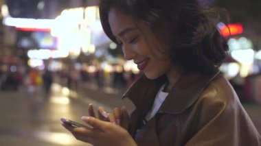 gece şehir caddesinde cep telefonu kullanarak güzel genç asyalı kadın, 4k