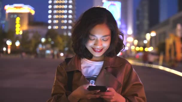 Bastante joven asiático mujer usando móvil en la ciudad calle en la noche, 4k — Vídeos de Stock