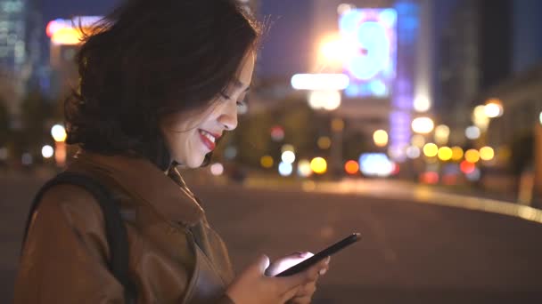 Bonita jovem mulher asiática usando telefone celular na cidade rua à noite, 4k — Vídeo de Stock