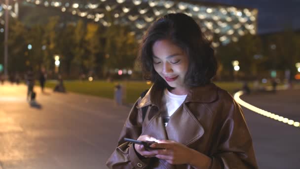 예쁜 젊은 아시아 여자 사용 휴대 전화 에 이 도시의 거리 에 밤, 4k — 비디오