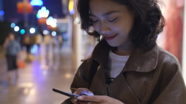 Bastante joven asiático mujer usando móvil en la ciudad calle en la noche, 4k — Vídeo de stock