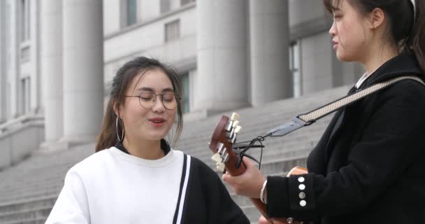 Een gitaar speler die een muziek voor haar zangeres vriend uit een gebouw — Stockvideo