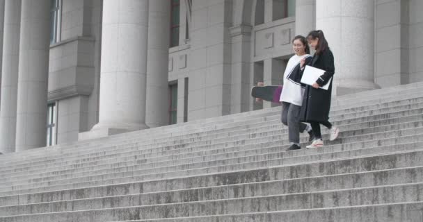 Дві молоді азіатські дівчата йдуть сходами, розмовляючи разом — стокове відео
