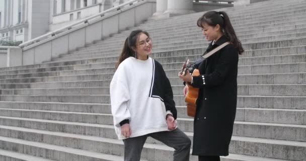 Young chinese girl playing the guitar and her friend singing on the steps — Wideo stockowe