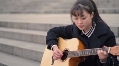 Bir genç asyalı kız gitar açık oynuyor