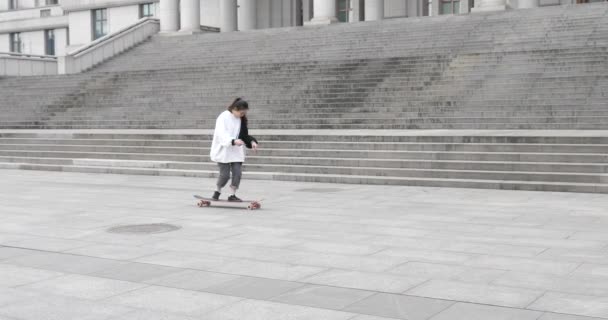 Jovem chinesa menina jogando truques em um skate no chão — Vídeo de Stock