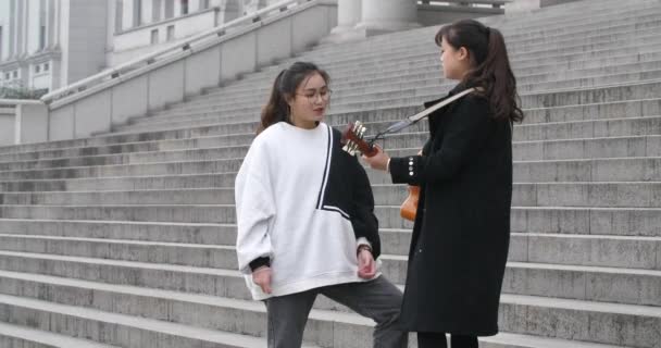 Menina chinesa feliz cantando uma música e seu colega tocando a guitarra — Vídeo de Stock