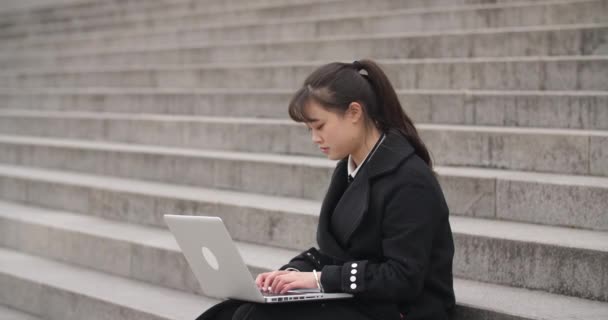 Açık havada oturan bir dizüstü bilgisayar ile çalışan genç çinli kız — Stok video