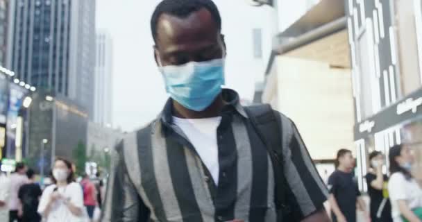 Black man wear mask walking in the street using mobile phone — Stock Video