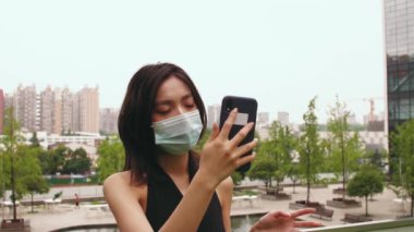 Maskeli bir kadın cep telefonuyla görüntülü sohbet ediyor.