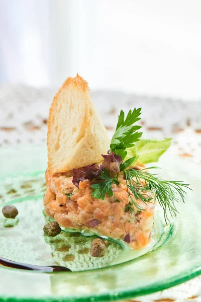 dish of salmon tartare with red and green onions and lemon zest with olive oil served on plate