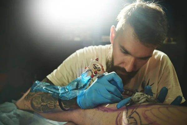 bearded tattoo artist making tattoo to client at workshop