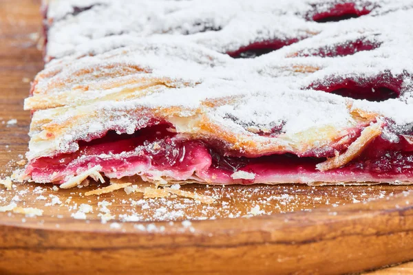 Slice of pie with cherries stuffing on wooden plate