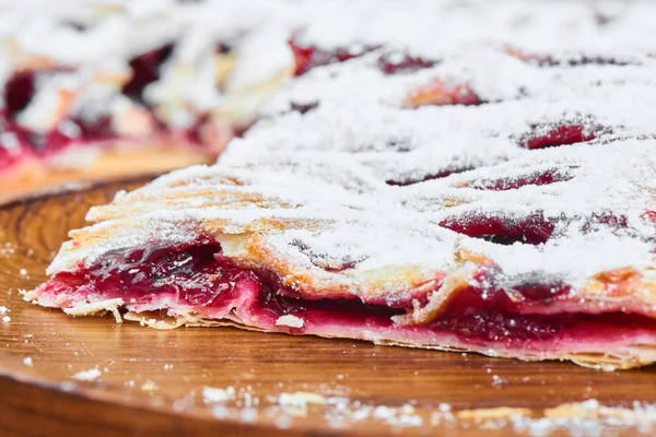 Slice of pie with cherries stuffing on wooden plate