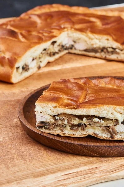 Slice of pie with chicken and mushrooms on wooden plate