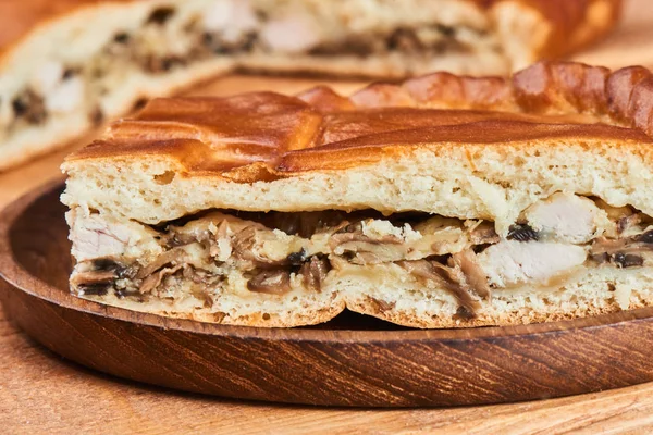 Slice of pie with chicken and mushrooms on wooden plate