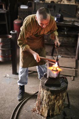 Örs üzerinde metal ürün üzerinden gaz brülörlü demirci ısıtır